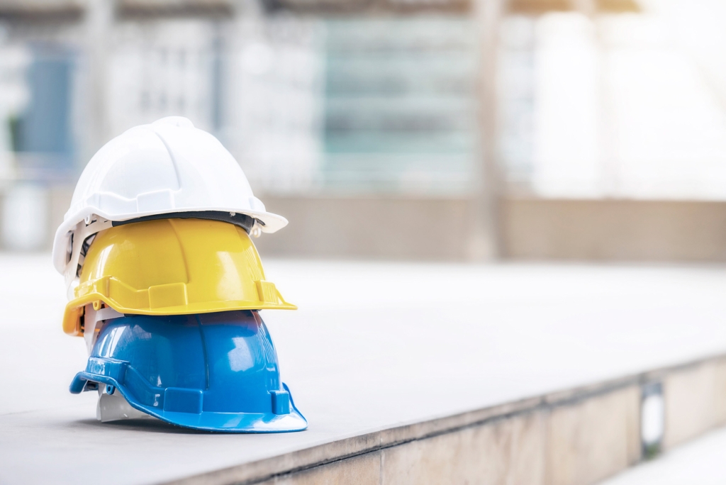 Hvit, gul og blå hard vernehjelm til arbeider, ingeniør eller besøkende liggende oppå hverandre på betonggulv i en by.